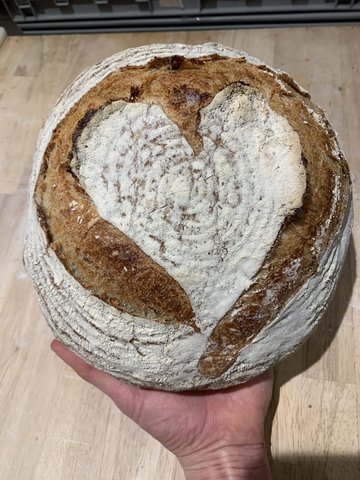 A heart-scored sourdough loaf held up in warm light