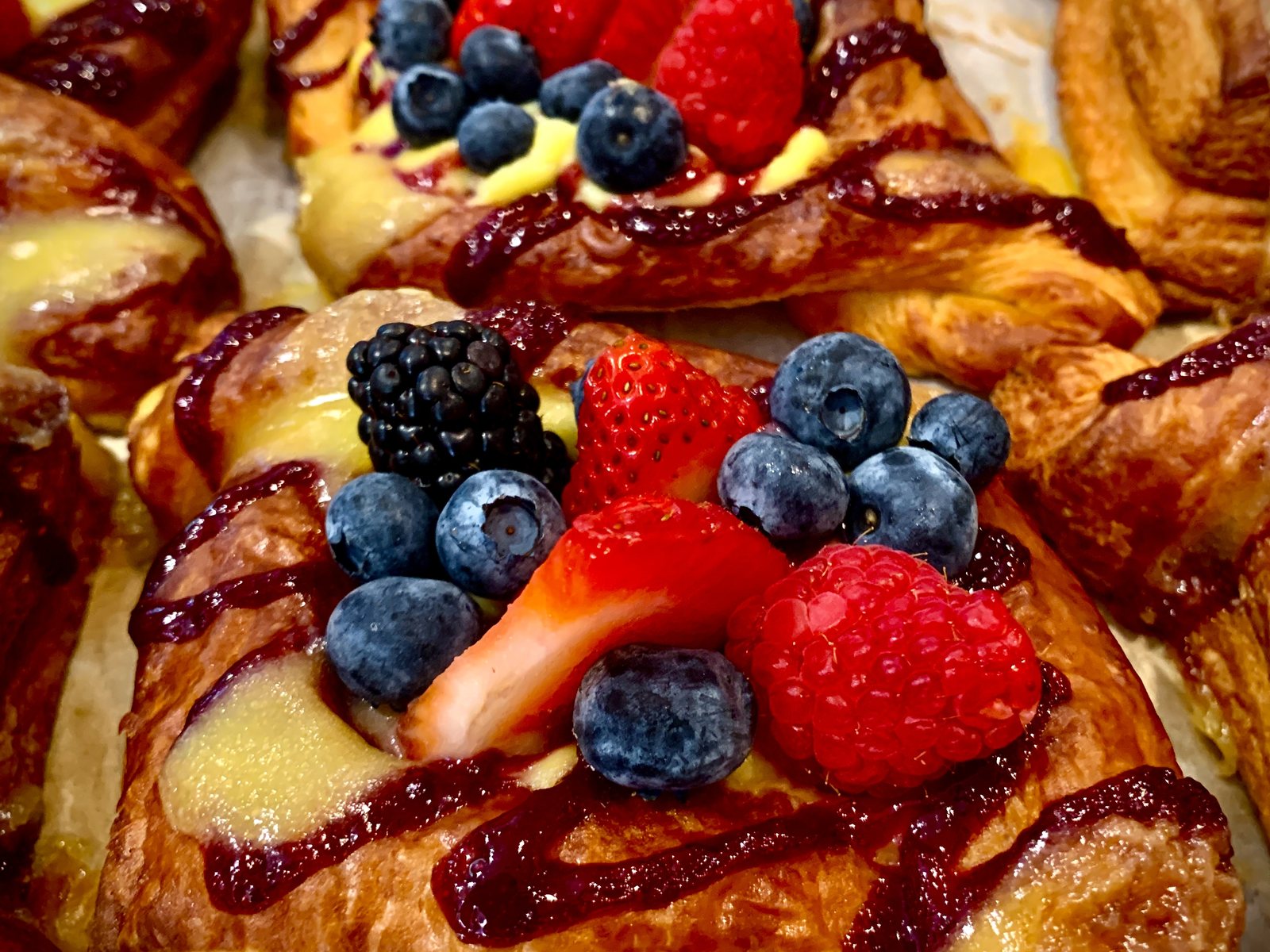 Laminated danish topped with strawberries, raspberries and blueberries over vanilla pastry cream